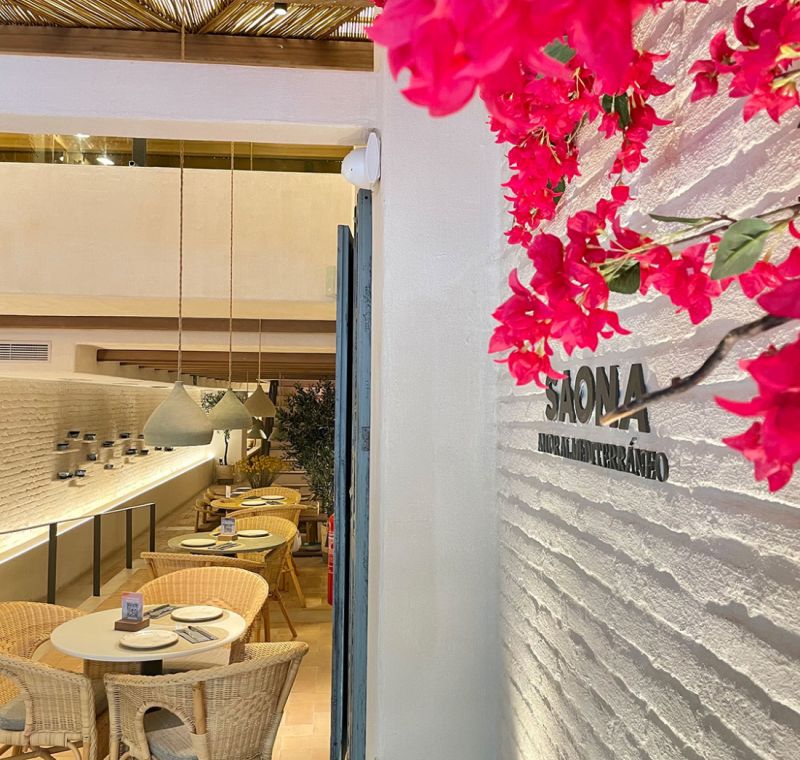 Greendecorum en Interior de Saona Restaurante con pared de ladrillo blanco, flores fuxia y puerta del comedor al fondo