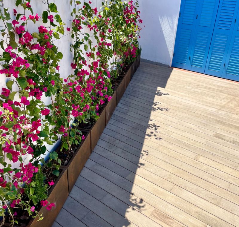 Terraza exterior de Barcelona Paralel con suelo de láminas, puerta azul y flores de color rosa en la pared blanca